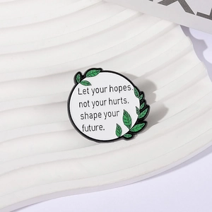 Broche minimaliste en émail blanc avec citation et feuilles vertes sur support texturé