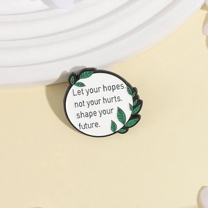 Broche ronde émaillée blanche minimaliste avec motif de feuilles vertes et texte inspirant