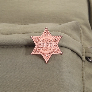 Detailed close-up of rose gold Sheriff badge pinned to a green canvas bag