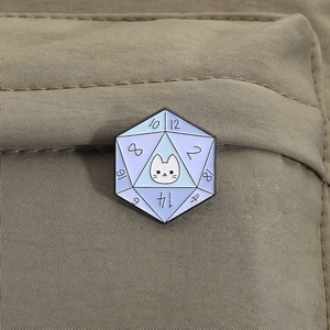Detail of a D20 cat enamel pin with blue gradient on a khaki canvas background