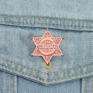 Close-up of rose gold sheriff star badge with relief engraving on denim fabric