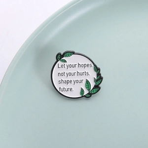Minimalist enamel brooch with 'Let your hopes shape your future' quote and green leaf