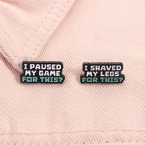 Macro shot of two enamel pins with funny slogans on pink denim fabric background