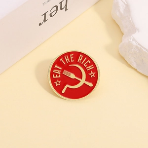 Dettaglio della spilla smaltata rossa e oro EAT THE RICH con emblema forchetta e falce