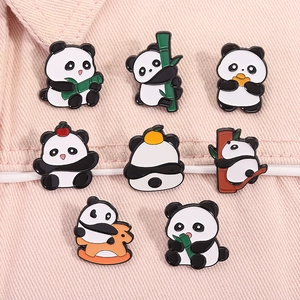 Flat lay of eight cute cartoon panda enamel pins featuring bamboo and apple motifs on fabric