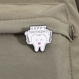 Cute enamel tooth pin with Happy Toothdsay slogan on dark green fabric texture