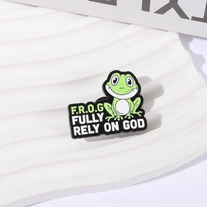 Cartoon green frog enamel pin with 'Fully Rely On God' text on white display stand