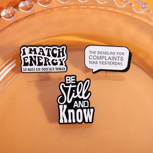 Close-up of three black and white enamel letter pins on a decorative orange tray
