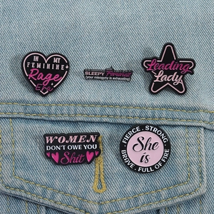 Detailaufnahme von feministischen Emaille-Pins in Rosa auf einer blauen Jeansjacke