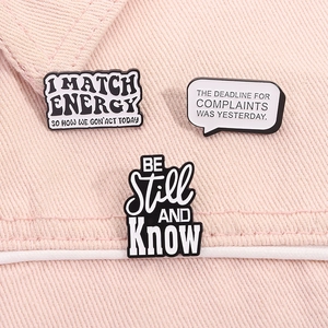 Detailed shot of three black and white enamel pins with quotes on pink denim fabric