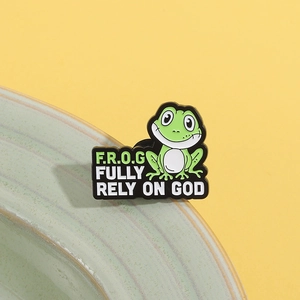 Cartoon frog enamel pin with Fully Rely On God quote leaning on green ceramic