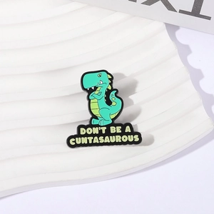 Funny green dinosaur enamel pin with Don't Be a Cuntasaurous quote on white stand