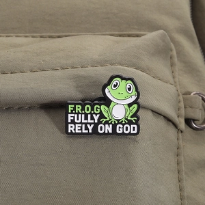 Gros plan du pin's grenouille émaillée verte avec texte F.R.O.G sur un sac en toile