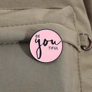 Détail du pin's rond en émail rose avec texte BE YOU TIFUL sur un sac en toile