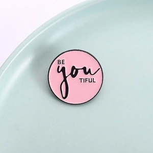 Vue rapprochée du pin's émaillé rose avec texte BE you TIFUL motivant en noir