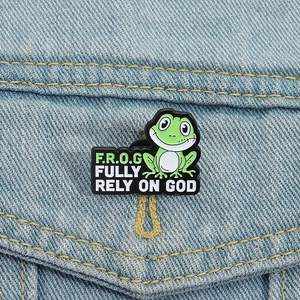 Détail d'un pin's grenouille verte sur veste en jean avec texte Fully Rely On God