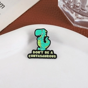 Cute green dinosaur enamel pin with 'Don't Be A Cuntasaurous' text on white plate