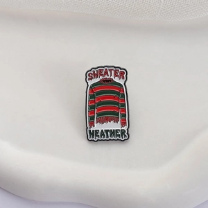Detailed enamel pin featuring iconic red and green striped sweater and horror movie font