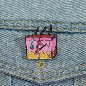 Detailed skin anatomy enamel pin with hair follicle layers on blue denim jacket