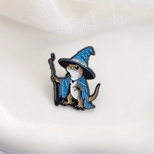 Spilla smaltata a forma di lucertola mago con tunica blu e bastone su tessuto bianco