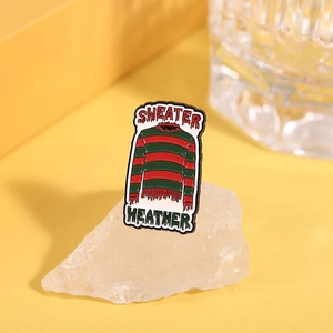 Close-up of red and green striped enamel pin with 'Sweater Weather' text on crystal base