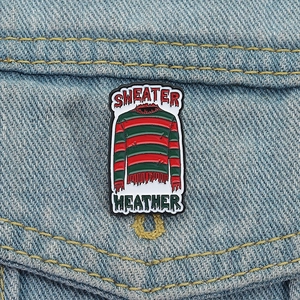 Detail of red and green striped Freddy sweater enamel pin with Sweater Weather text