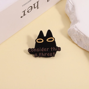 Detail of black enamel cat pin with yellow eyes and 'consider this a threat' text