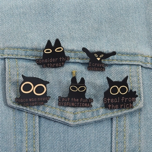 Set of five black enamel cat pins with gold eyes pinned on a denim jacket pocket