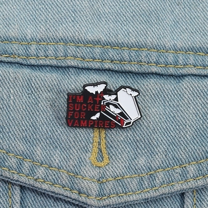Detail of vampire-themed enamel pin with red gothic letters on a blue denim jacket