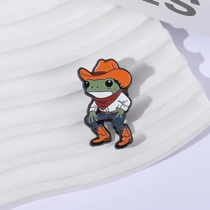 Pin's en émail grenouille cowboy avec chapeau orange et foulard sur fond blanc texturé