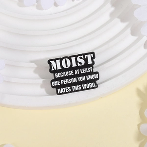 Humorous enamel pin featuring black metal badge with white text about hating the word moist