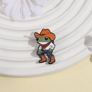 Broche grenouille en émail portant un chapeau de cow-boy orange sur fond blanc