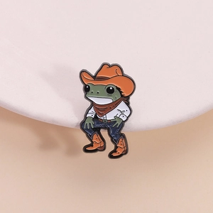 Broche grenouille cowboy en émail avec chapeau orange sur un support d'exposition