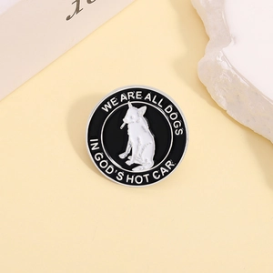 Détail d'un pin's rond en émail noir avec un chien et texte WE ARE ALL DOGS IN GOD'S HOT CAR