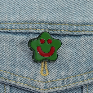 Close-up of green star enamel pin with a red smiley face on light blue denim jacket