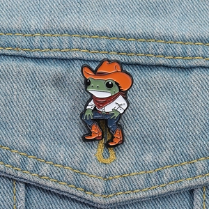 Détail d'un pin's en émail grenouille cowboy fixé sur une texture de tissu en denim bleu