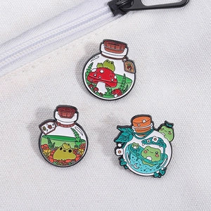 Three cute enamel pins featuring frogs in bottles pinned to a white canvas bag