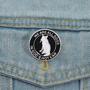 Gros plan d'un pin's émaillé de chien blanc sur denim avec texte We Are All Dogs In Gods Hot Car