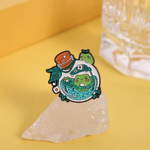 Detailed close-up of a cute cartoon frog enamel pin in a glass bottle on white stones