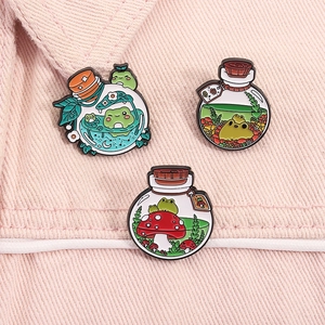 Detailed view of three cute frog enamel pins pinned on pink denim fabric material