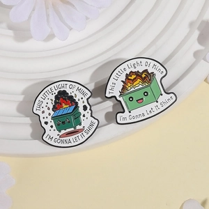 Cartoon dumpster fire enamel pins with motivational quotes on a white decorative tray