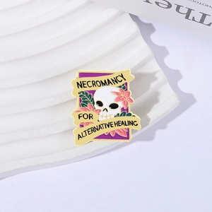 Enamel skull brooch with pink flowers and Necromancy lettering on a white pedestal