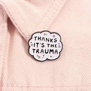 Cloud enamel pin with Thanks It's The Trauma quote on a pink textured fabric background