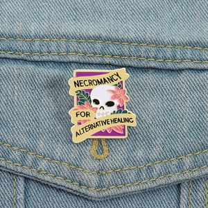Necromancy enamel pin with skull and pink flowers on a blue denim jacket pocket