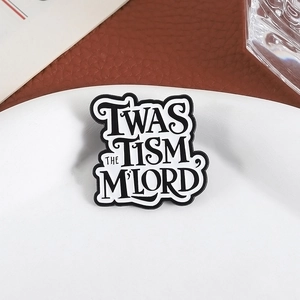 Dettaglio della spilla smaltata con testo 'TWAS THE TISM M'LORD' su piatto di ceramica