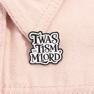 Dettaglio della spilla smaltata con scritta 'TWAS THE TISM M'LORD' su denim rosa