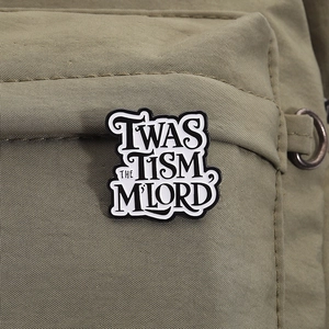 Dettaglio della spilla smaltata 'TWAS THE TISM M'LORD' su borsa in tela verde oliva