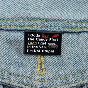 Black enamel pin with funny quote and candy icon pinned on light blue denim fabric