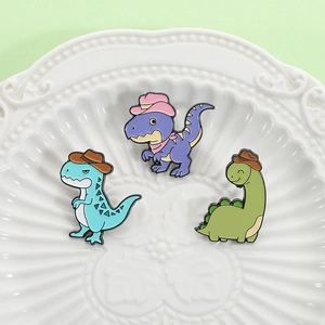 Three cute cartoon dinosaur enamel pins with cowboy hats on a decorative white ceramic plate