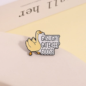 Detail view of yellow enamel goose pin with 'GASLIGHT GATEKEEP GOOSE' text on warm background
